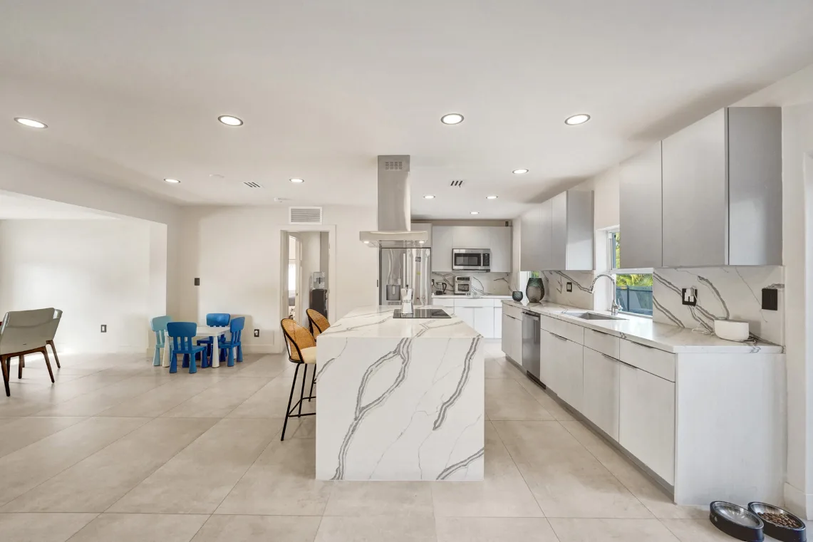 Open-concept white kitchen with marble waterfall island beside a bright family room